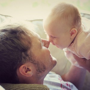 Happy Young Father is Playing with his newborn baby girl at home, and kissing noses together. Vintage style color filter.