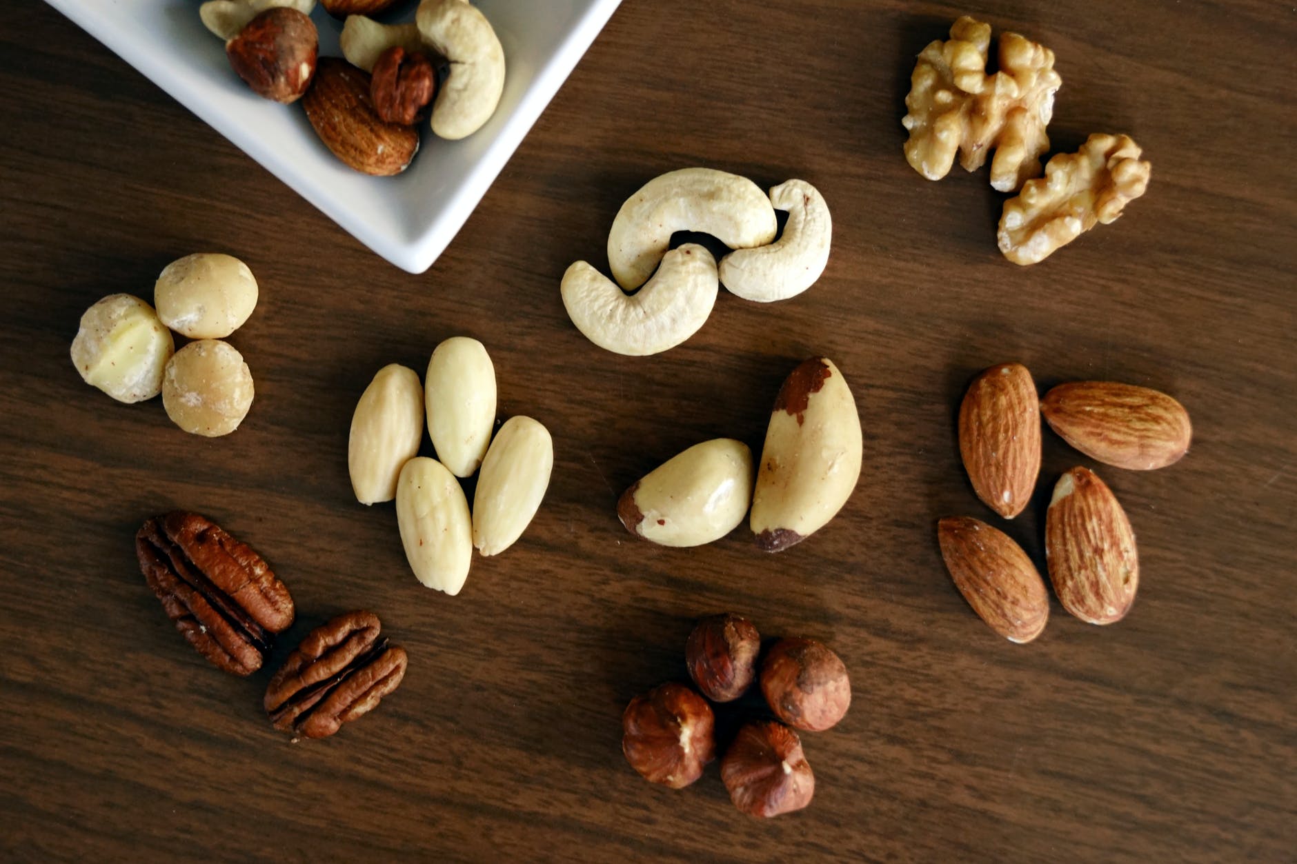 Mesa de madeira escura com nozes, castanhas e grãos sortidos espalhados. Os cereais e grãos são indicados para diabéticos e pré-diabéticos por serem alimentos com baixo índice glicêmico.