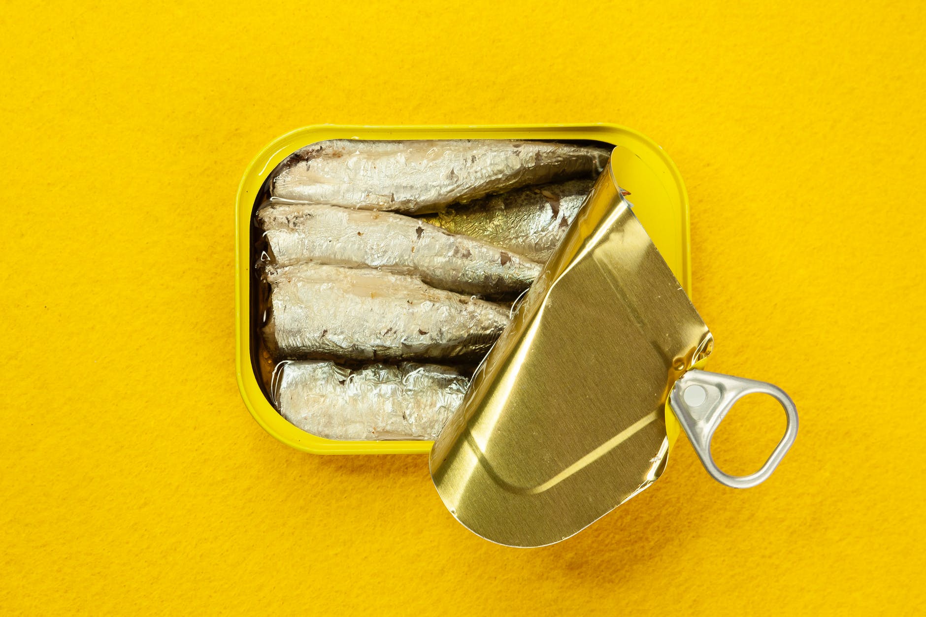 Sardinha em lata pode ser usada em diversas receitas. A lata de sardinha está aberta sobre uma mesa de cor amarela.