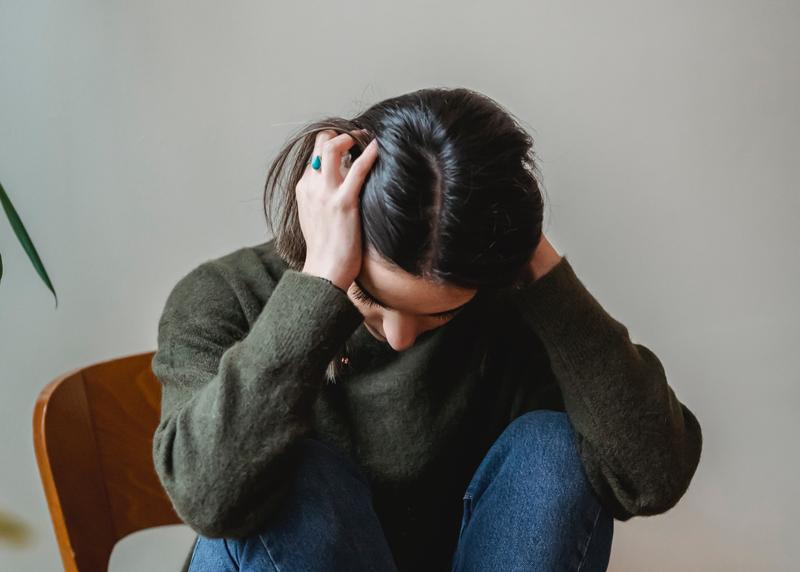 Mulher branca está sentada com as mãos tapando o ouvido. A escuta de música alta pode afetar a saúde auditiva.