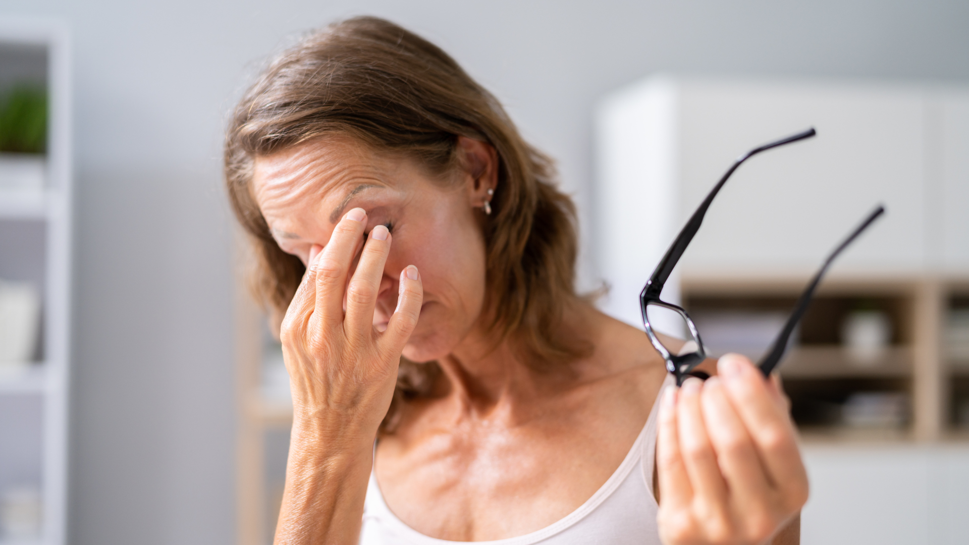 Mulher segurando os óculos e coçando os olhos